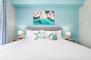 Un dormitorio con cama, dos mesitas de noche con lámparas, una obra de arte en la pared y una ventana con cortinas.