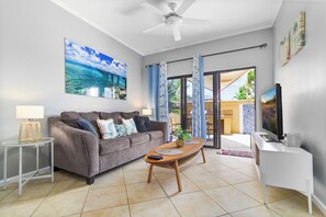 A living room with a sofa, coffee table, TV, and a painting of a beach scene.