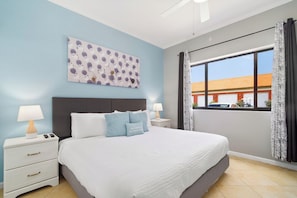 Camera da letto con un letto, comodini, un'opera d'arte appesa al muro, una finestra con tende e vista su un edificio.