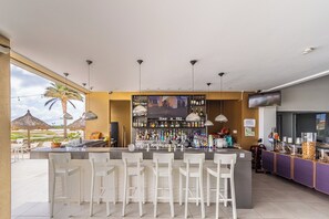 Una zona de bar con una barra alargada, varios taburetes y una variedad de botellas y vasos.