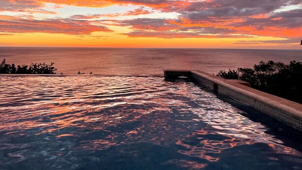 Une piscine avec vue sur l’océan et un ciel au coucher du soleil.