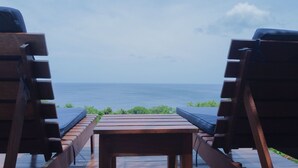 Une terrasse en bois avec deux chaises longues donnant sur l’océan.