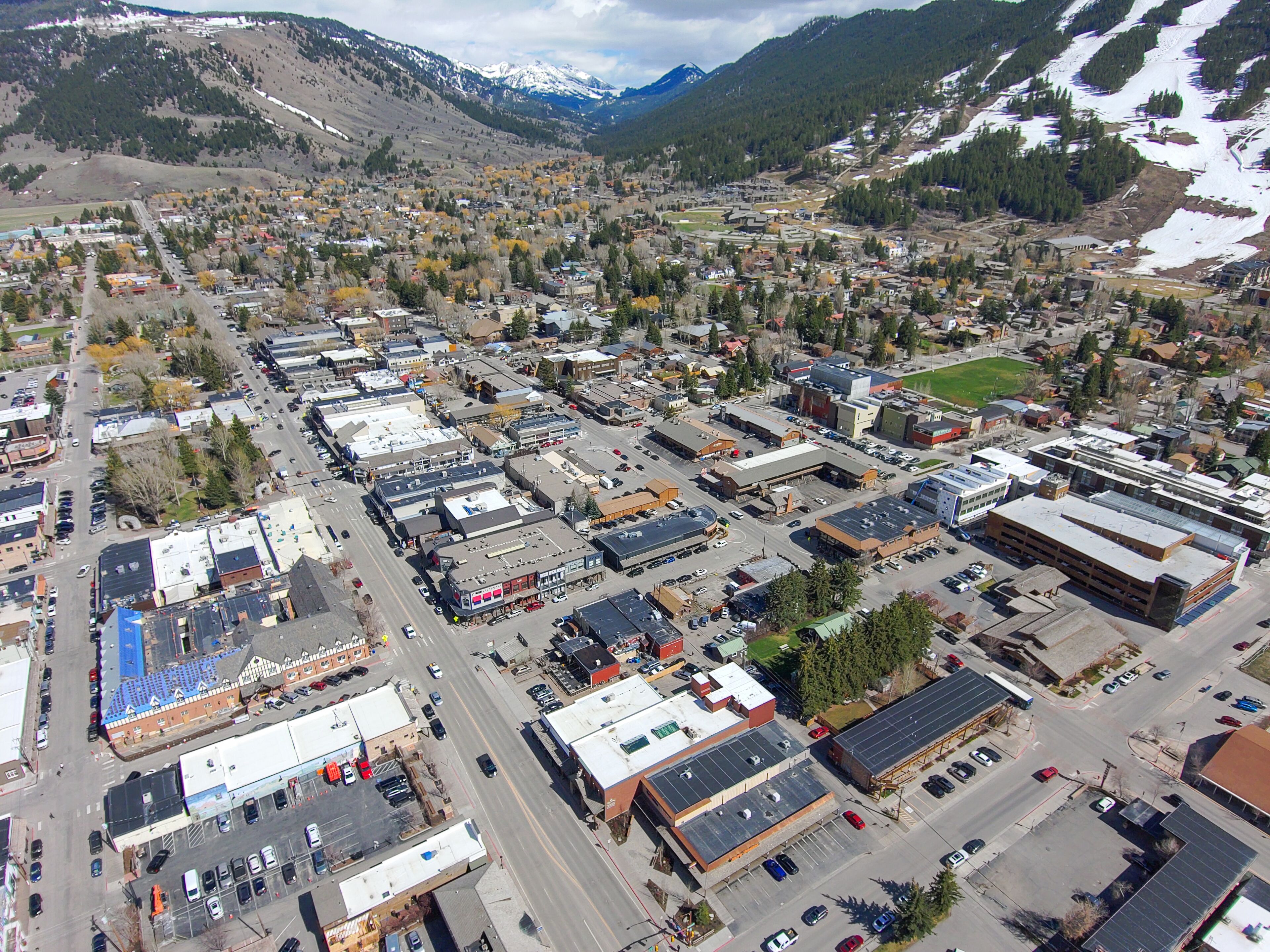 An aerial view of a town with a mix of commercial and residential buildings, roads, and a mountainous backdrop.