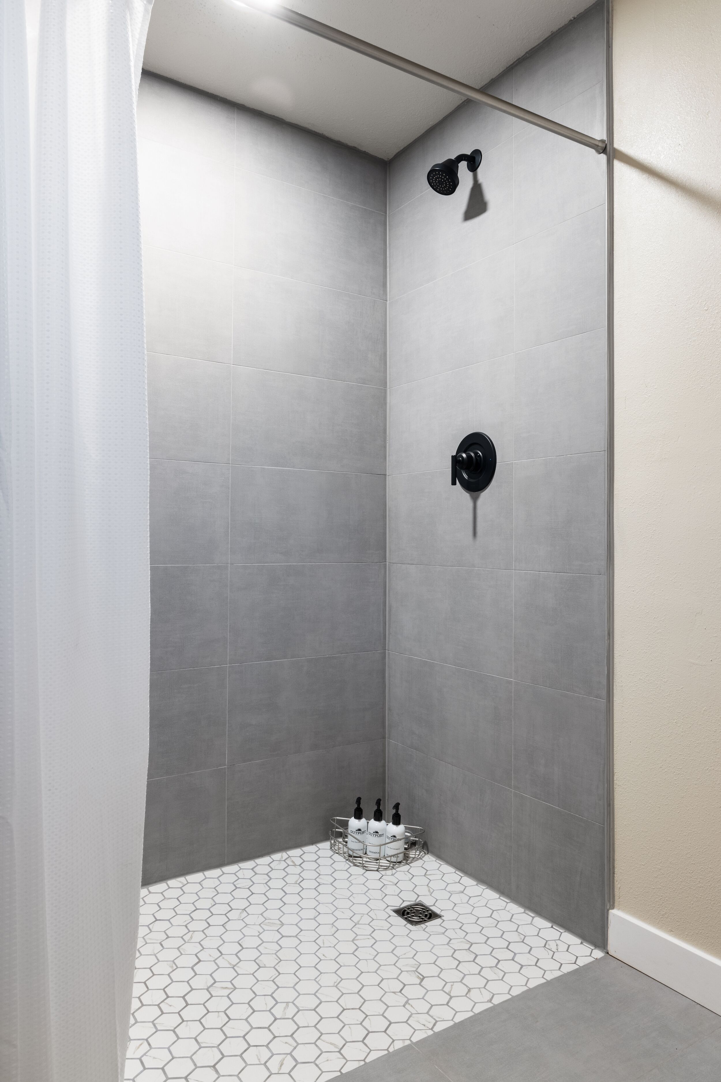 Une douche aux carreaux gris, un pommeau de douche et une petite étagère avec des articles de toilette.