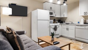 Una cocina moderna con armarios blancos, horno empotrado y microondas. Hay una mesa de madera con un control remoto y una planta en maceta.