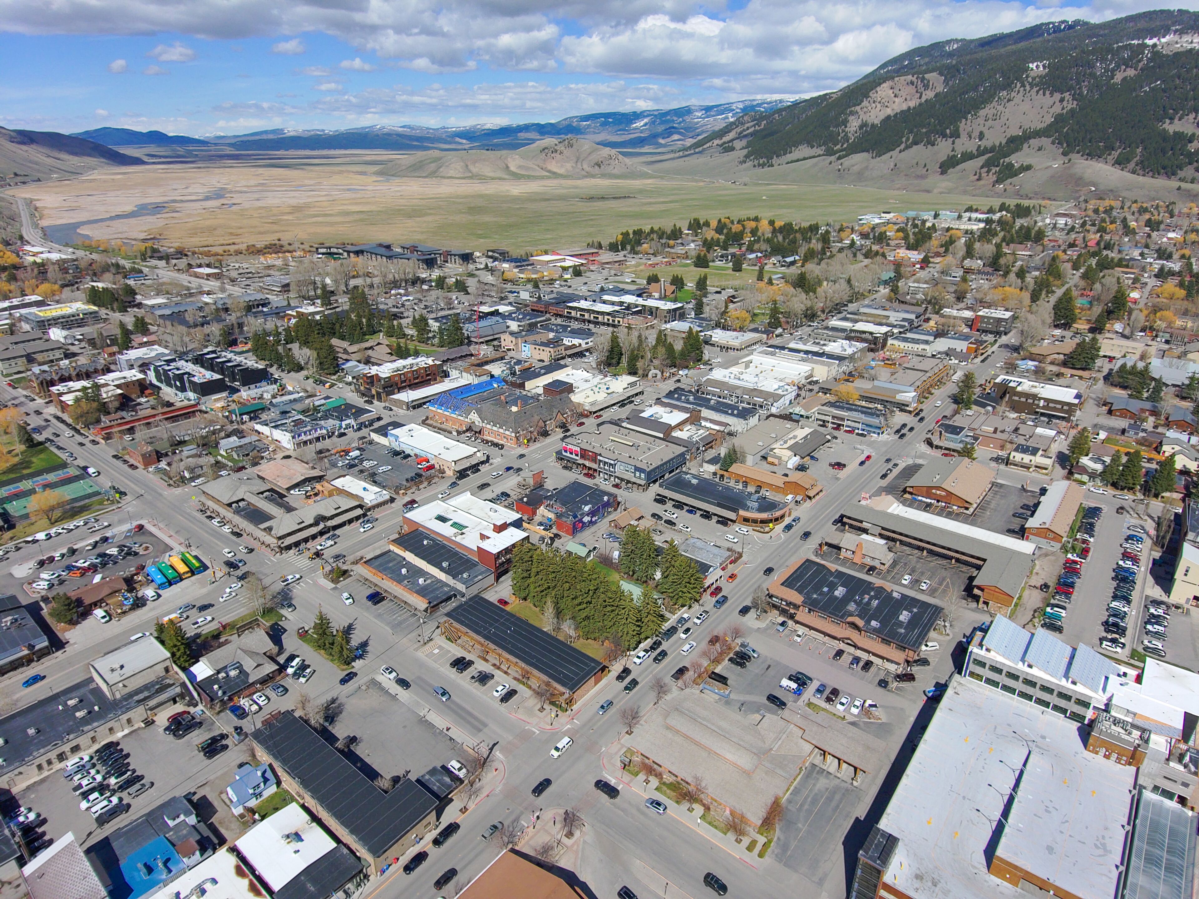 An aerial view of a town with a mix of commercial and residential buildings, roads, and a mountainous backdrop.