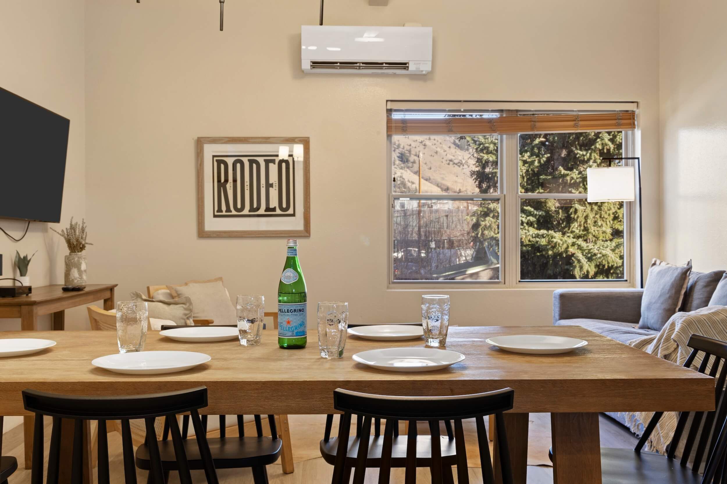 A dining area with a wooden table set for four, a bottle of Pellegrino water, and a framed 'RODEO' sign on the wall.