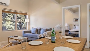A dining area with a wooden table set for four, a bottle of S.PELLEGRIO wine, and a view of a living room with a sofa and a window overlooking trees. - Outpost: Town Square Lodge 8 - Close to Town Square (Jackson)