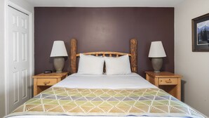 Une chambre à coucher avec un lit, deux tables de chevet avec des lampes, une tête de lit en bois et un tableau accroché au mur.