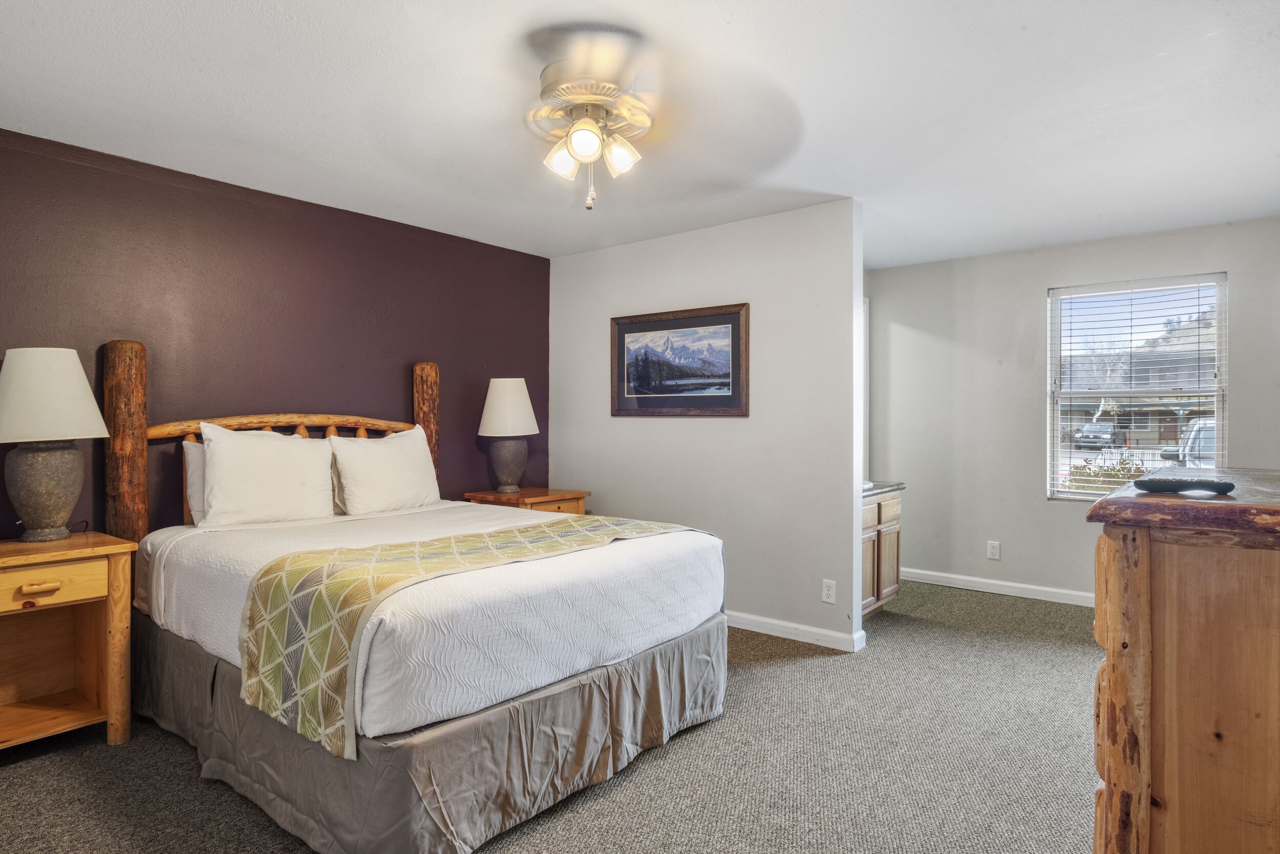 A bedroom with a bed, nightstands, a lamp, a ceiling fan, a window, and a picture on the wall.