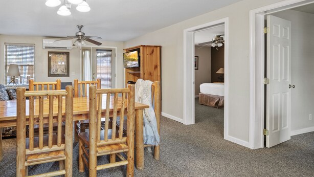 Un coin repas avec une table et des chaises en bois, un ventilateur de plafond et un téléviseur posé sur une commode en bois.