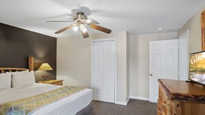 Ein Schlafzimmer mit einem Bett, einem Deckenventilator, einem Nachttisch mit Lampe und einer Holzkommode.
