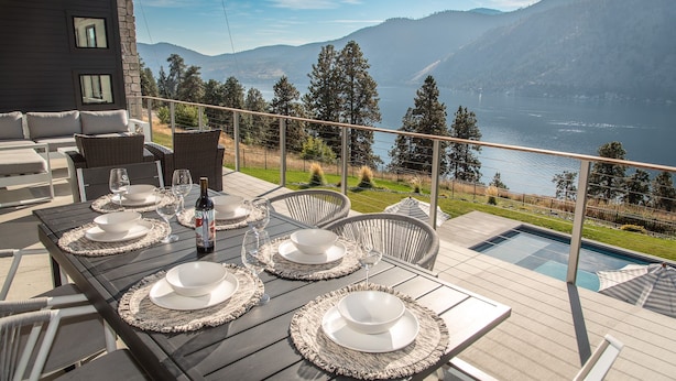 A dining table set for four with white plates, bowls, and wine glasses, overlooking a lake and mountains. - Private Pool | Stunning lake & mountain views | Modern, costal design (Manson)
