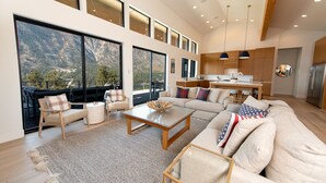 A spacious living area with a large sofa, a coffee table, and a view of mountains through large windows. - Private Pool | Stunning lake & mountain views | Modern, costal design (Manson)