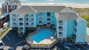 A beachfront hotel with a pool, multiple balconies, and a view of the ocean.