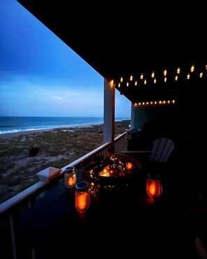 A balcony with a view of the beach, a fire pit, and string lights. - Oceanfront&Pool,Huge Shaded Deck 9+family seating&swing,linens,beachchairs, toys (Carolina Beach)