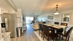 A spacious kitchen with a large island, a dining area with a wooden table and chairs, and a view of the living room through an open door.