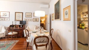 A dining area with a table set for four, surrounded by chairs. There are framed pictures on the walls, a television on a wooden cabinet, and a lamp above the table. - ELEGANT COZY 2BD IN SANTA CROCE - FLORENCE (FIRENZE)