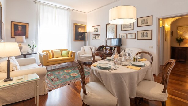 A well-lit living room with a dining area, featuring a sofa, chairs, a table set for dining, and various framed pictures on the walls. - ELEGANT COZY 2BD IN SANTA CROCE - FLORENCE (FIRENZE)