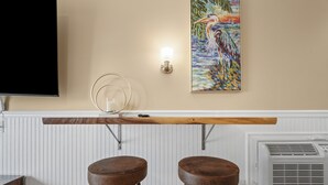 Una zona de bar con dos taburetes, un televisor, una lámpara fijada a la pared y un cuadro.