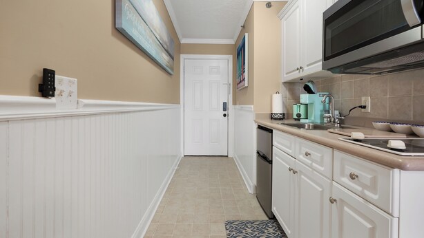 Una cocina con armarios blancos, un microondas, una cafetera y una puerta al fondo.