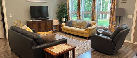 A living room with a sofa, armchair, TV, and a plant.