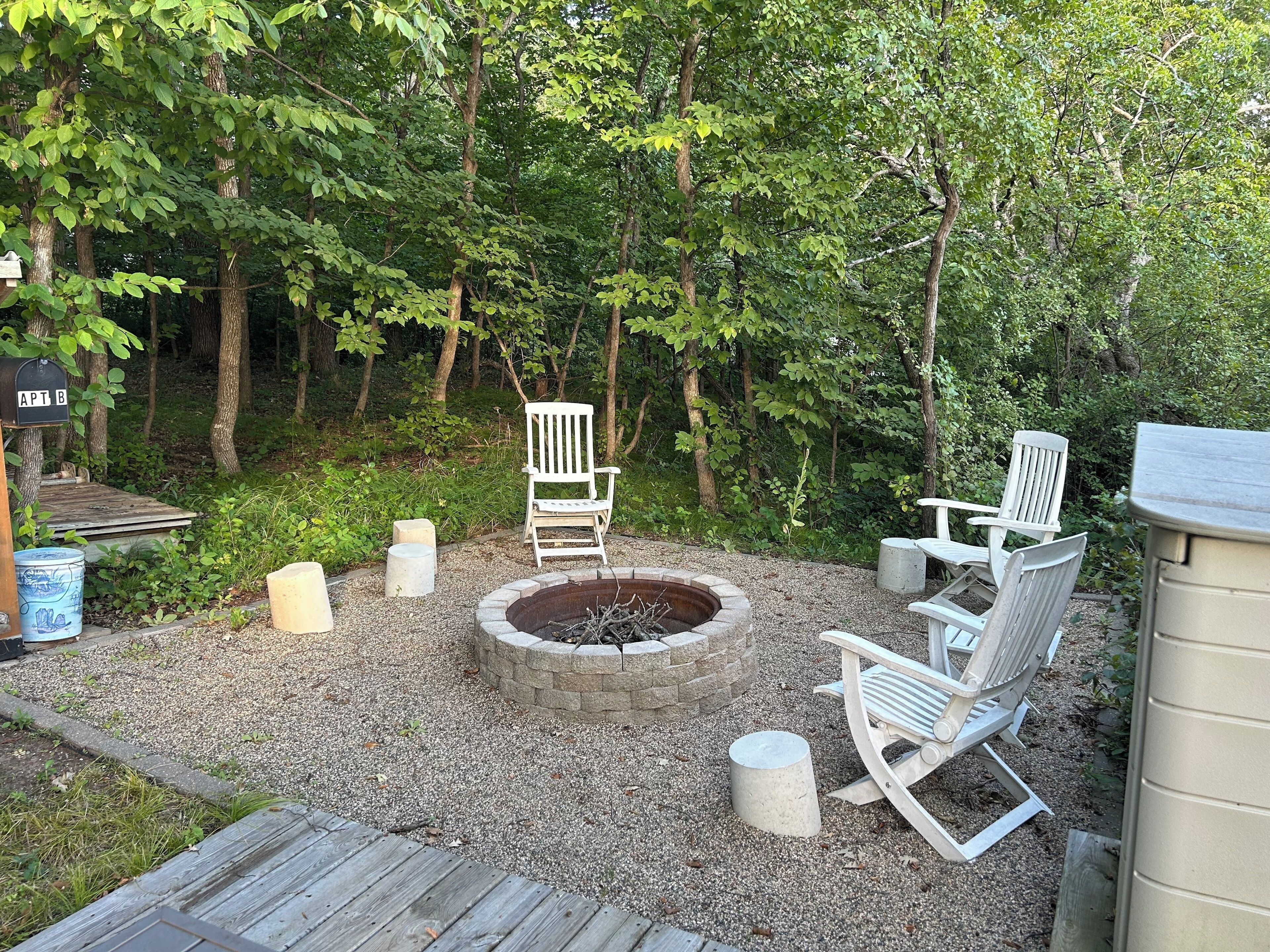 A backyard with a fire pit, white Adirondack chairs, and a mailbox labeled 'APT B'.