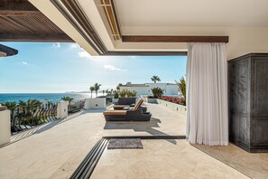 Uma área externa iluminada pelo sol com piscina, espreguiçadeiras e vista para o mar.