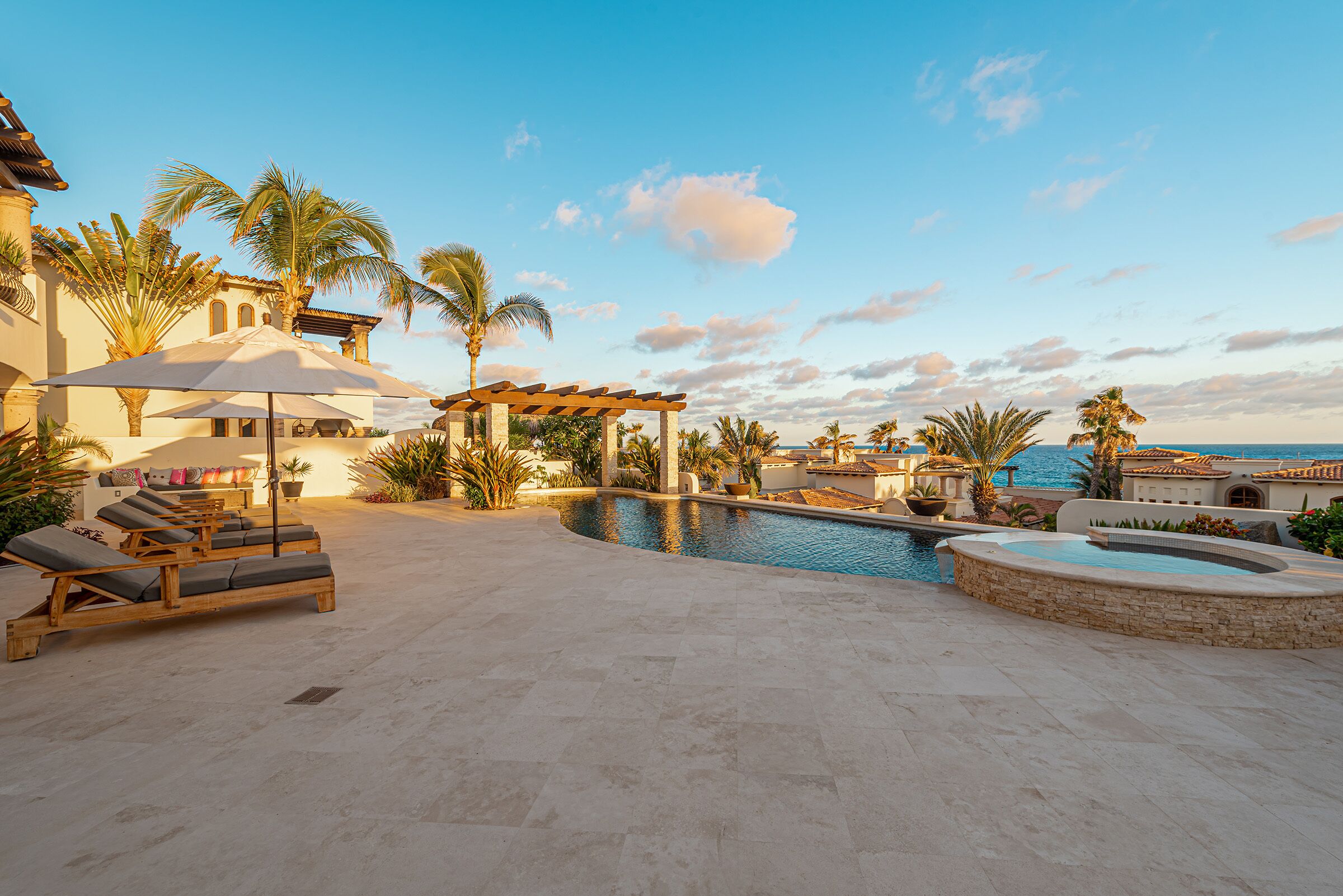 A pool area with lounge chairs, a pergola, and a hot tub.