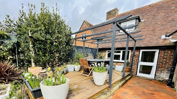A patio with a wooden deck, potted plants, and a metal pergola structure. - A quirky character cottage on the edge of the New Forest (Totton)