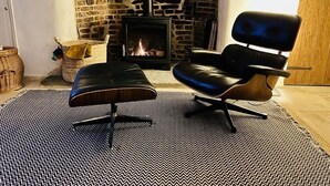 A living room with a fireplace, a black leather sofa, and a patterned rug. - A quirky character cottage on the edge of the New Forest (Totton)