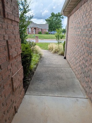 A brick pathway leading to a garage with a brick wall on one side and a grassy area on the other.