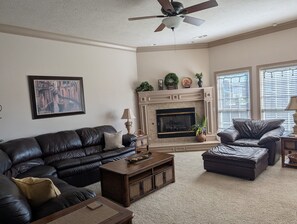 A living room with a fireplace, leather furniture, and a ceiling fan.