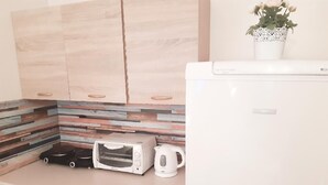Een keuken met een magnetron, broodrooster en waterkoker op het aanrecht, houten kastjes en een plantje op het werkblad.