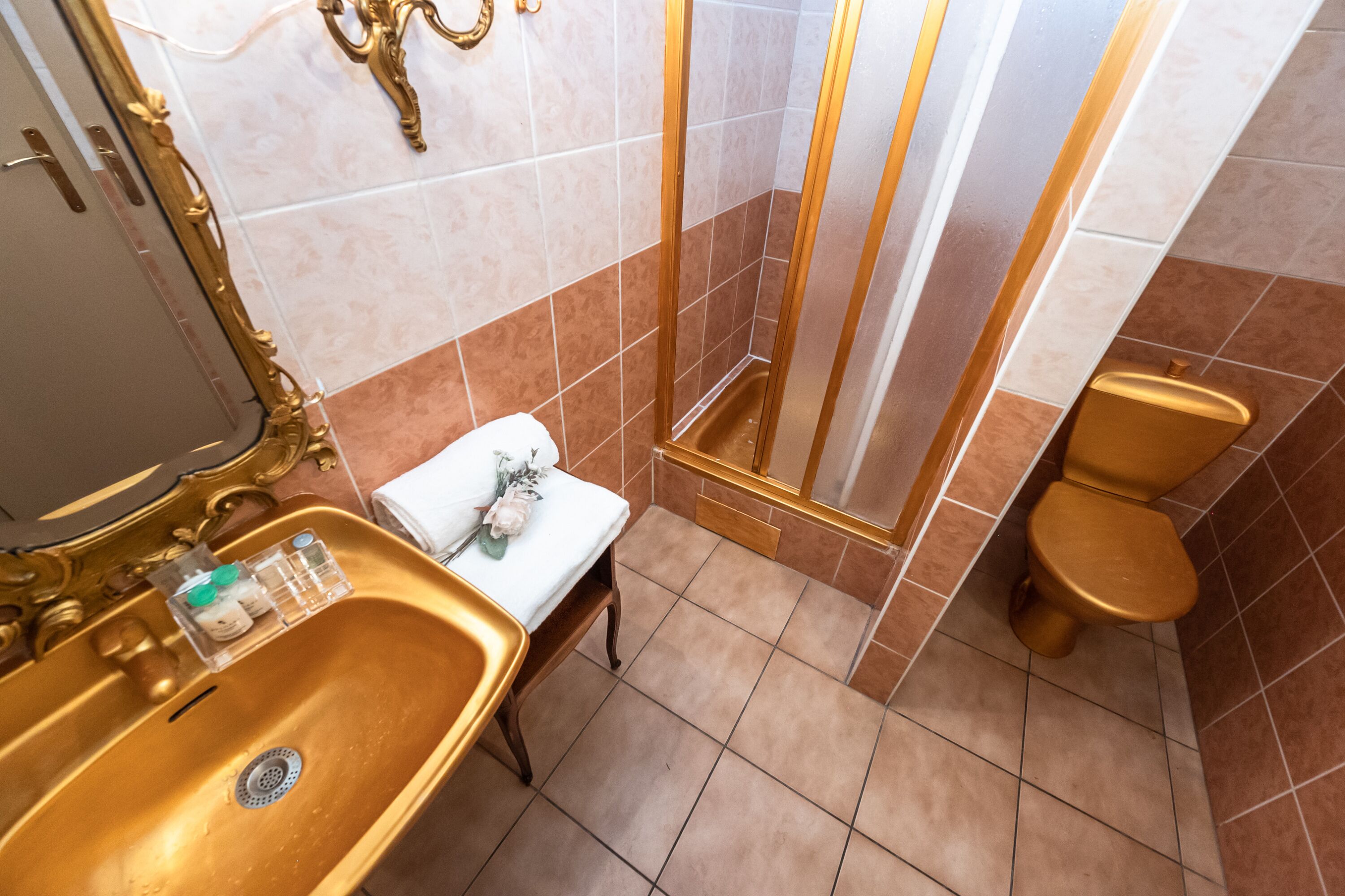 Un bagno con lavandino dorato, wc bianco e doccia con dettagli dorati.