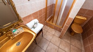 Een badkamer met een gouden wastafel, een wit toilet en een douche met gouden details.