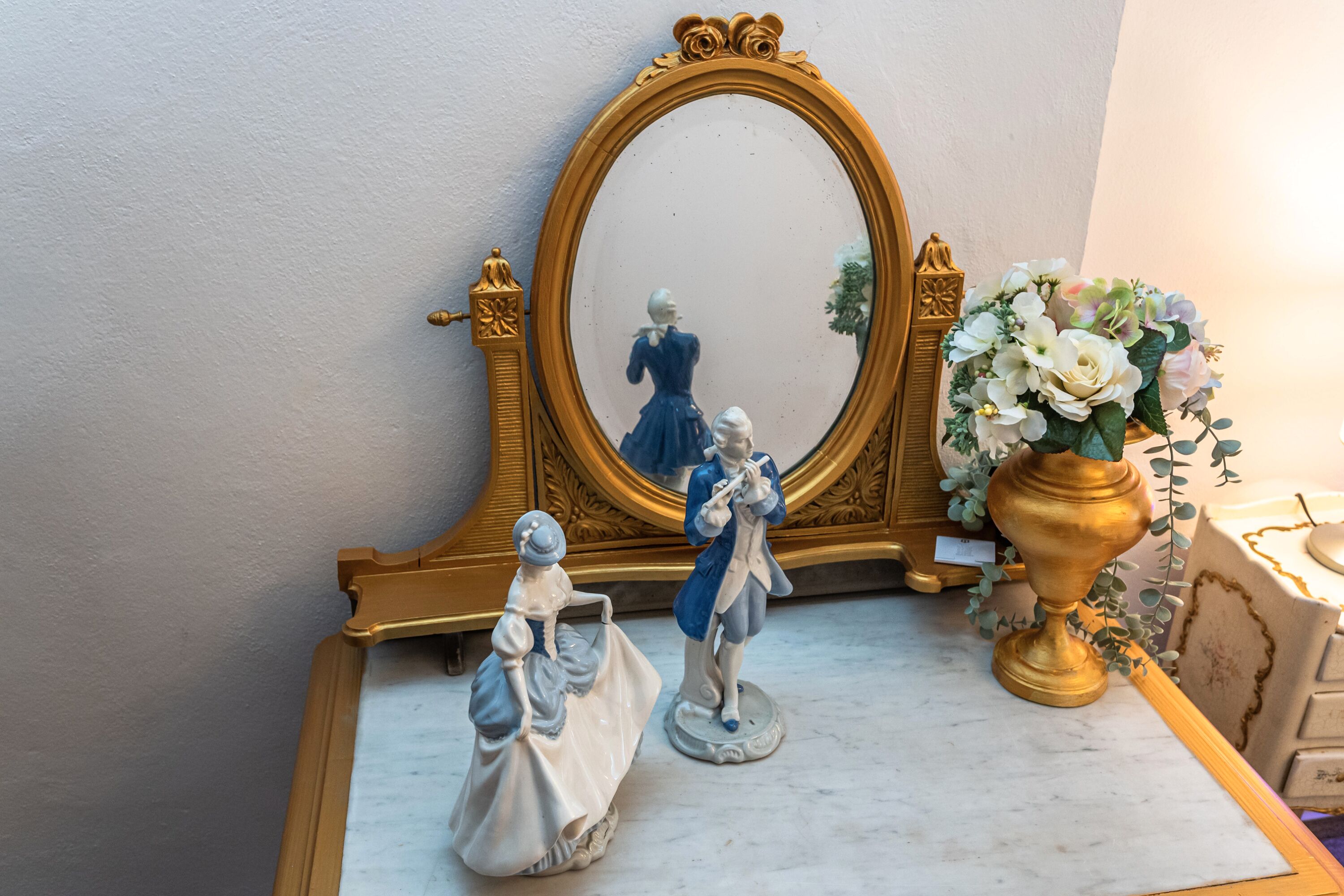 Ein Marmortisch mit einem goldgerahmten Spiegel, einer Vase mit weißen Blumen und zwei Figuren.
