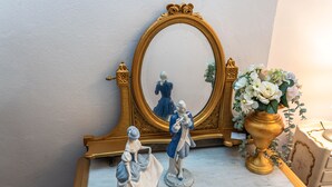 Een marmeren tafel met een spiegel in gouden lijst, een vaas met witte bloemen en twee beeldjes.