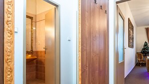Een gang met een houten deur, een badkamer met douche, en een kerstboom in de verte.