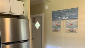 Una cocina con un refrigerador de acero inoxidable, piso de madera y una mesa de comedor con sillas. Se ve una puerta de salida al fondo.