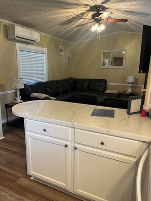 A compact living space with a kitchen area, a black leather sofa, and a ceiling fan. - Visit Fernandina Beach/Amelia Island and surrounding areas (Yulee)