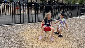 Un parque infantil con un módulo de juegos de madera y una cerca de metal negro.