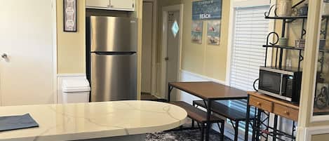 A kitchen with a central island, bar stools, a refrigerator, and a microwave.