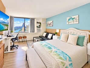 A modern hotel room with a large bed, a desk, a laptop, a chair, a sofa, and a view of a cityscape.