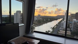 A room with a large window overlooking a river and cityscape at sunset. - Waikiki Ocean&Sunrise View Studio (Honolulu)