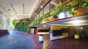 A spacious indoor area with a checkered floor, a reception desk, and a wooden staircase with greenery. - Waikiki Ocean&Sunrise View Studio (Honolulu)