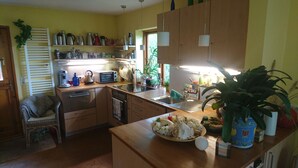 Una cocina compacta con tostadora, hervidor y varios electrodomésticos. Hay un lavamanos, una encimera con un cuenco de flores y una planta en maceta.