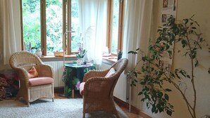 Una habitación acogedora con sillas de mimbre, una mesita pequeña y un ventanal con cortinas.