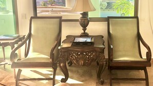 A room with two upholstered chairs, a small table with a lamp, and a view of the ocean through large windows.
