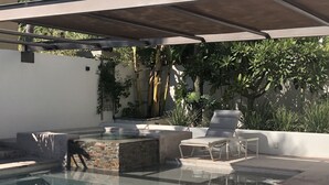 A swimming pool with a stone accent wall, a lounge chair, and a covered patio area.